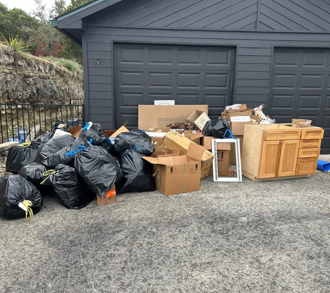 Driveway piled with trash bags, boxes, and old cabinets before removal