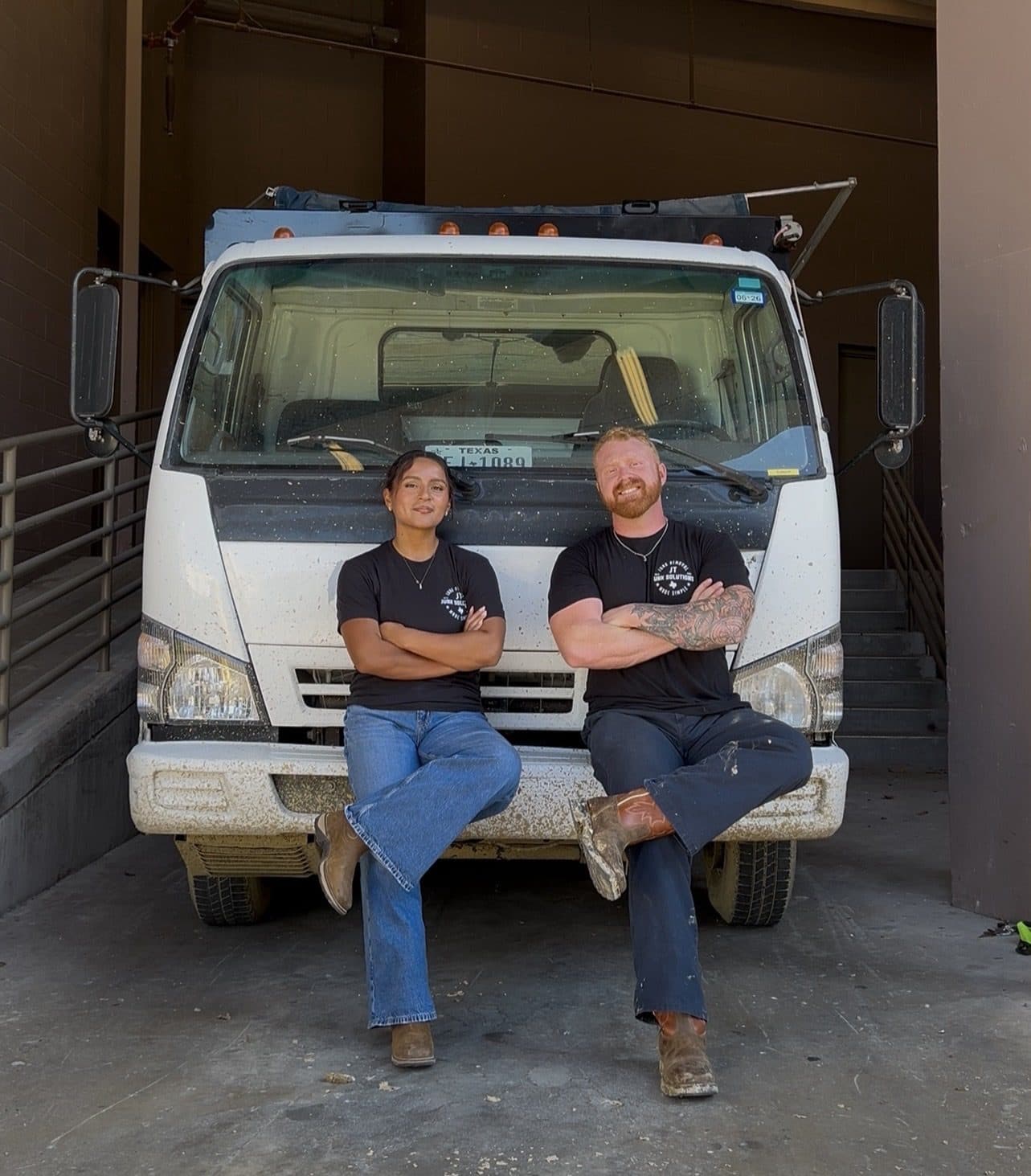 Tanner and Jackie, owners of JT Junk Solutions, sitting on the bumper of the JT truck